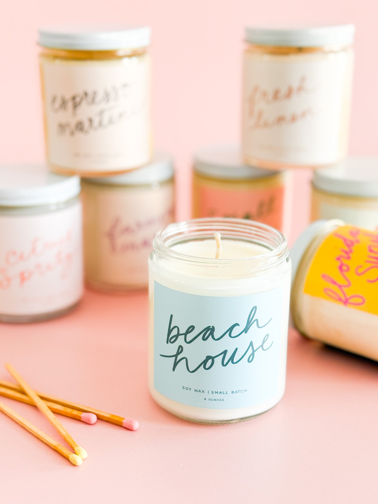Beach House soy candle with colorful Poured Goods candles and matches on a pink background