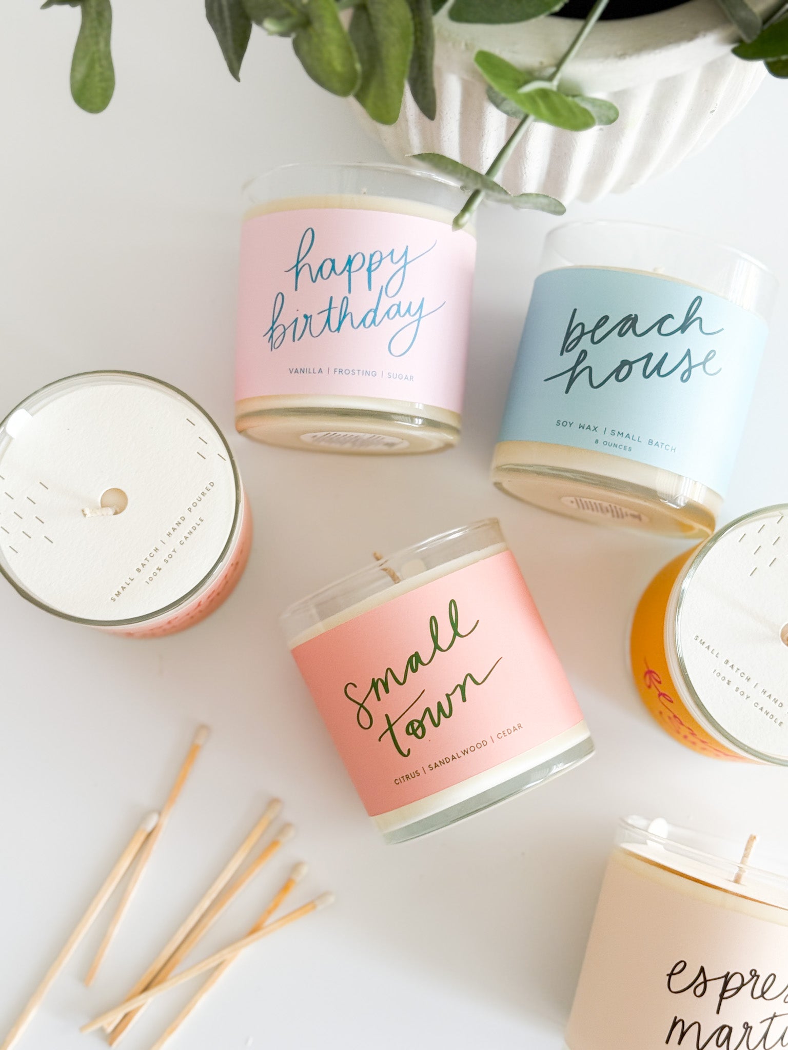 Poured Goods glass candles with pastel labels, greenery and matches