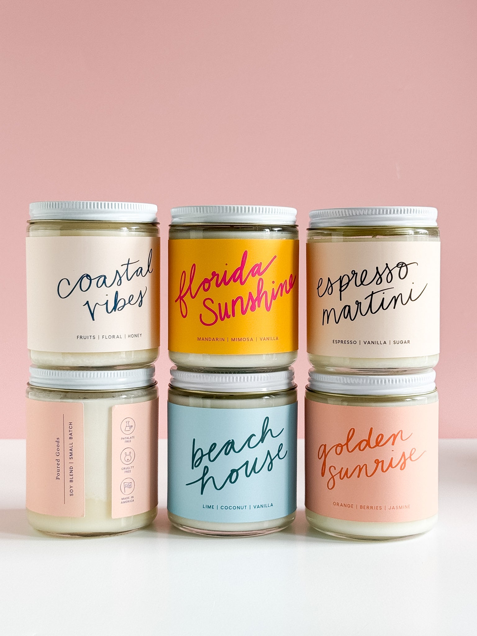 Colorful Poured Goods jar candles stacked on a pink background